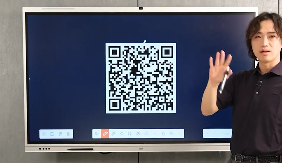 大型ディスプレイに表示されたQRコードの前で男性が手を挙げている。