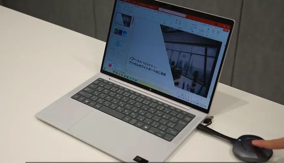 ノートパソコンにPowerPointプレゼン資料が表示されており、隣にワイヤレスプレゼンツールが接続されている。