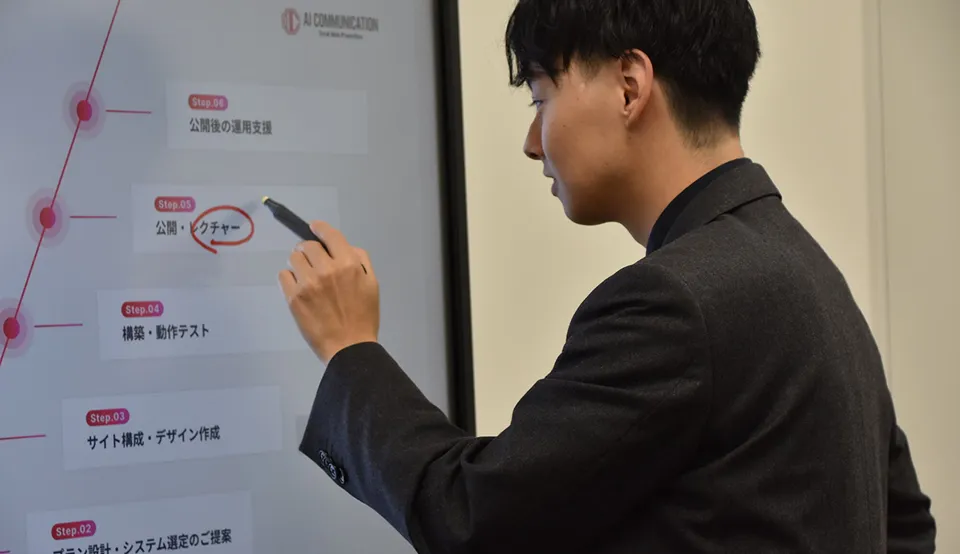 黒いスーツを着た男性がタッチパネルに表示された工程図を指している。