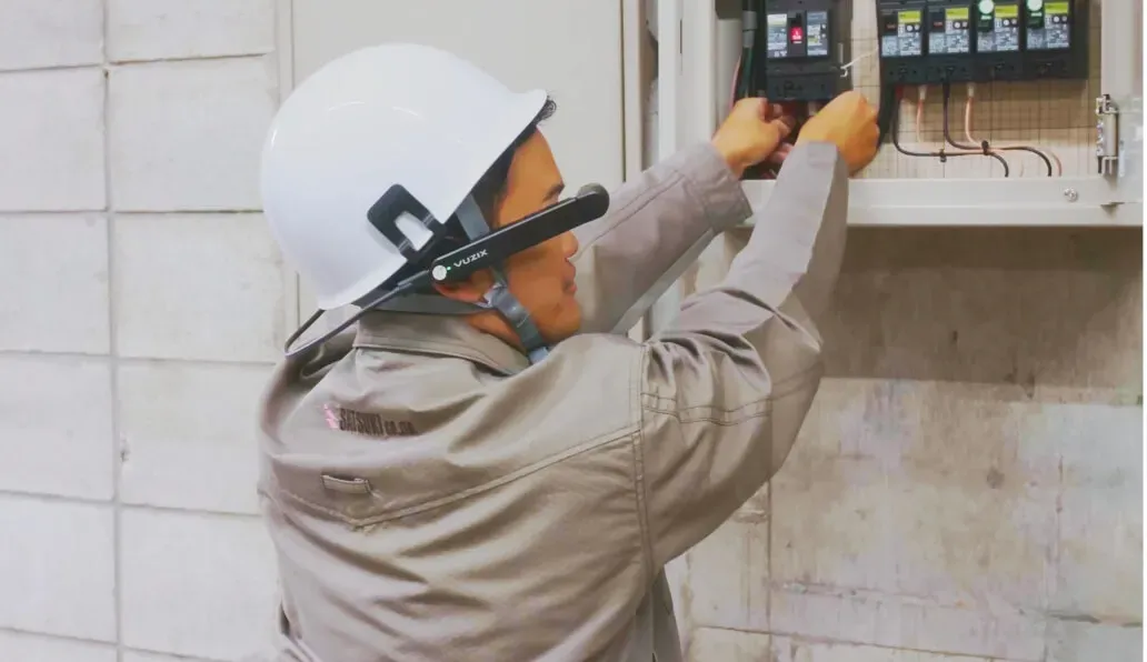 作業服とヘルメットを着用した作業員が配電盤で機器の調整を行っている様子