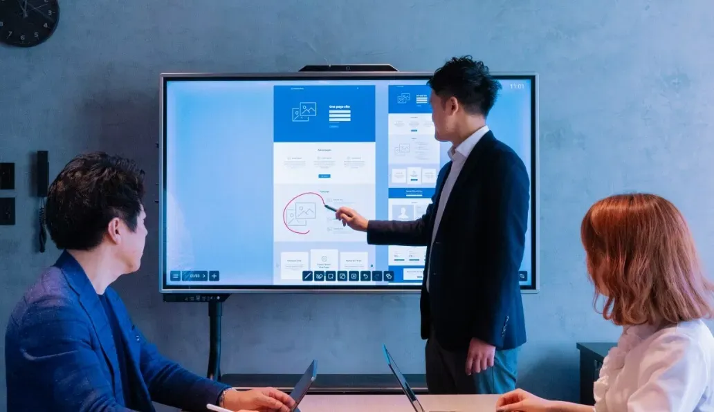 会議室で男性が大型ディスプレイに表示されたデザイン案を指しながらプレゼンする様子